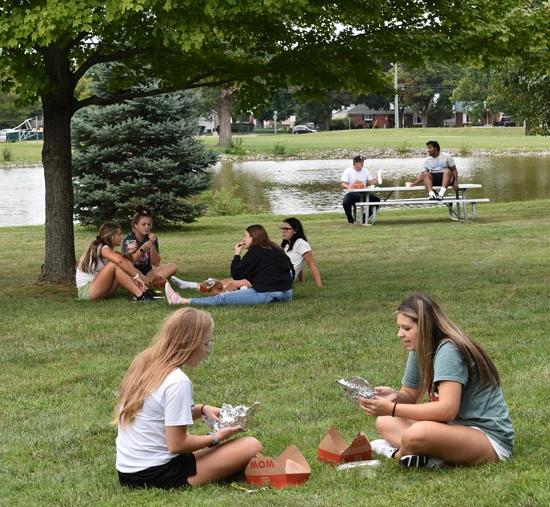 students sitting in the grass by the pond talking